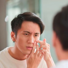 Man checking his face in the mirror to look for acne.