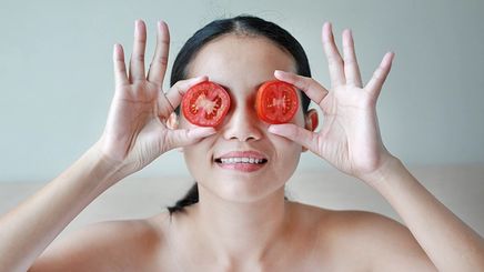 Asian woman putting tomato slices over eyes