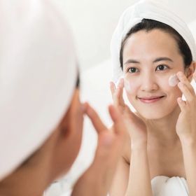 Asian woman in a bathroom applying face cream in front of a mirror. 