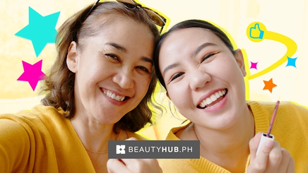 Asian mother and daughter in yellow, laughing while holding lip gloss