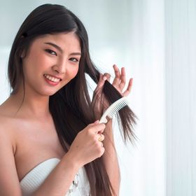 Woman brushing her long hair with a white comb.