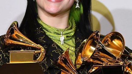 Billie Eilish wearing a middle part holding Grammy Awards.