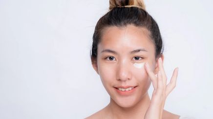Asian woman applying concealer under her eyes