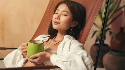 A woman closing her eyes while enjoying a cup of tea.