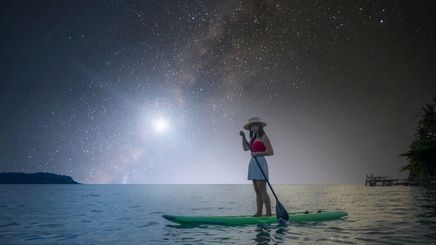 Asian woman on a paddle board under the moon and stars.