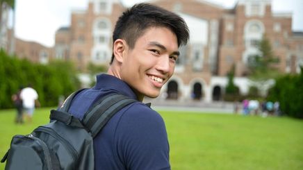 Asian man with a backpack smiling at the camera. 