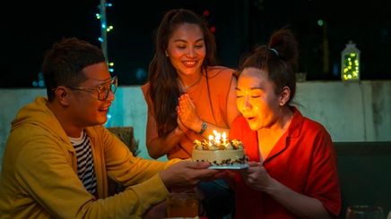 Asian woman blowing birthday cake with friends.