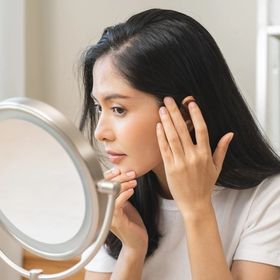 Woman checking her cheek and jawline in the mirror to see if she has PCOS acne.