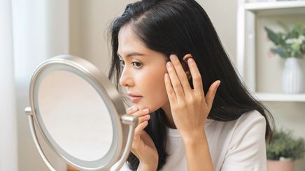 Woman checking her cheek and jawline in the mirror to see if she has PCOS acne.