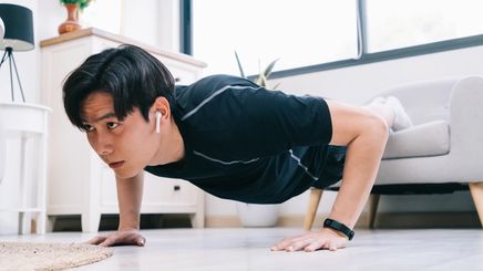 An Asian guy doing a push up by placing both feet on his couch at home  