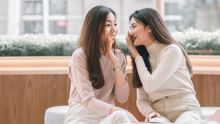 Two Asian woman gossiping at a coffee shop.