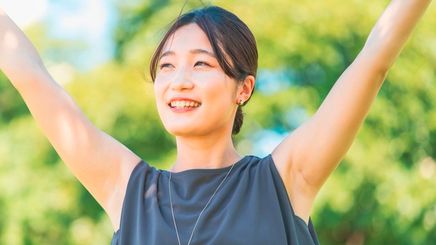 Asian woman with her arms raised outdoors.
