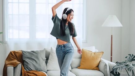 Woman listening to music through her headphones and dancing in the living room.