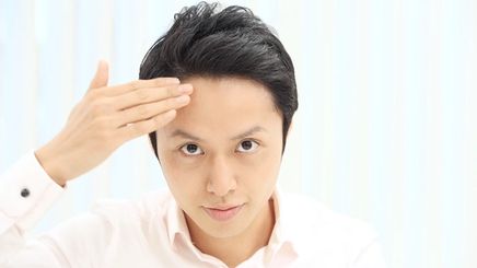 A young Asian man looking at hair and touching forehead.