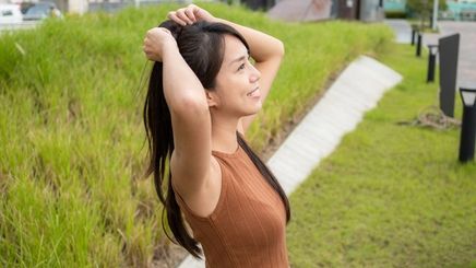 Asian woman tying hair into a high ponytail