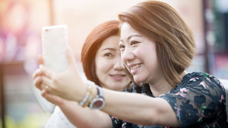 Photo of older Asian woman with a friend, taking a selfie.