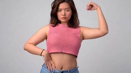 Confident Asian woman in pink knit cropped top and jeans