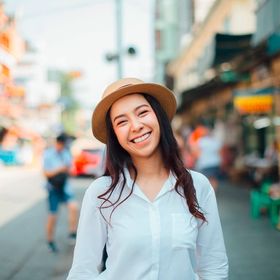 Asian woman in a hat standing outdoors on a sunny day.