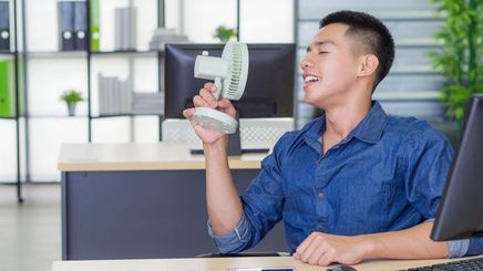 Asian man cooling himself with a fan 