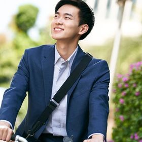 Young Asian man in a business suit riding a bike.
