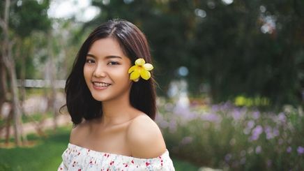 Asian woman with a flower pinned to her shoulder length hair.