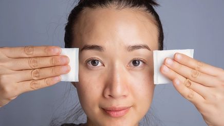 Asian woman cleanses skin with cotton pad
