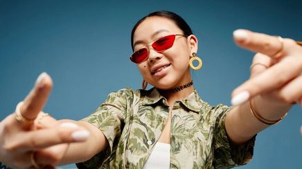 Asian Gen Z girl wearing red sunglasses, large earrings, and a printed shirt.