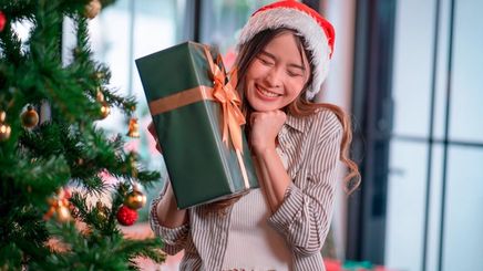 Giddy Asian woman holding a present beside a Christmas tree.