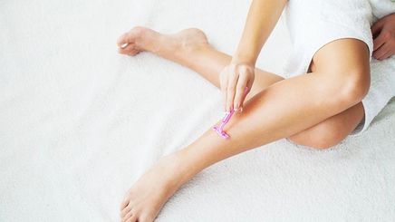 Woman using a pink razor to shave her legs.