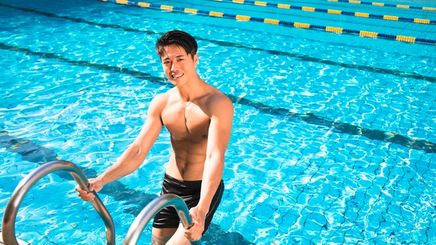 Smiling Asian man climbing out of pool.