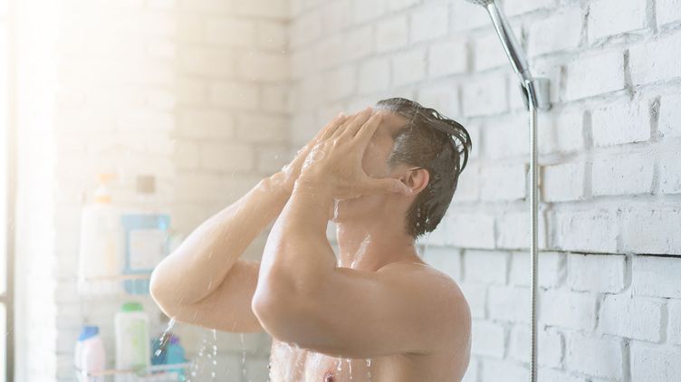 A man takes a shower inside his bathroom.