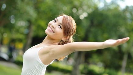 A beautiful Asian woman in a white tank tap raising her arms outdoors