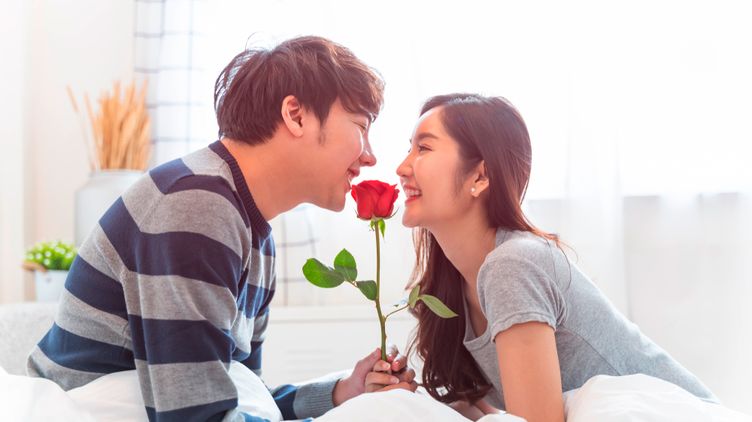 A portrait of woman and man holding a rose while gazing at each other lovingly.
