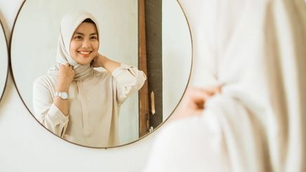 Asian woman in hijab looking at mirror.