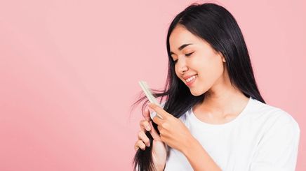 Asian woman combing her hair against pink background