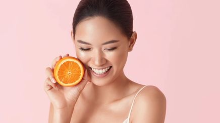 Smiling Asian woman holding half an orange 
