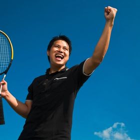 Asian man in black shirt playing tennis.