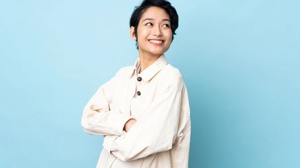 An Asian woman with androgynous hair cut wearing a white shirt against a blue background 