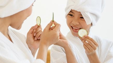Asian mom and child wearing white robes and holding cucumber slices