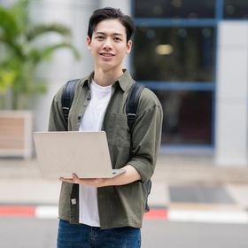Young Asian man with a backpack holding a laptop.