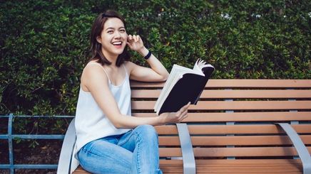 Asian woman smiling while sitting on a park bench holding a book