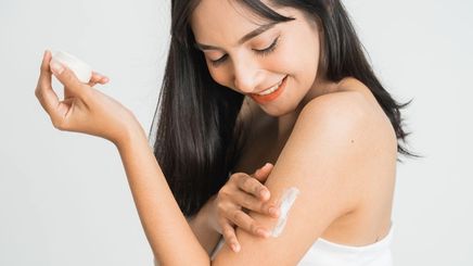 A woman applying lotion to her arm.