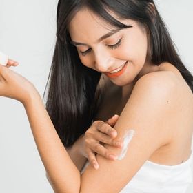 A woman applying lotion to her arm.