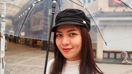 Asian woman in newsboy cap holding clear umbrella.