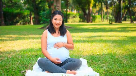 A portrait of pregnant woman cradling her baby bump at a park.