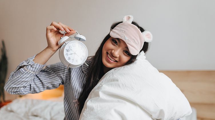 Asian woman in pajamas holding an alarm clock