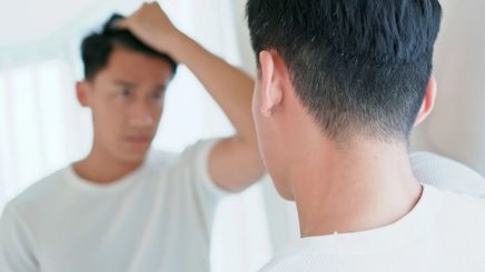 Asian man touching his hair in front of a mirror.