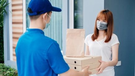 Woman with facial mask receiving packages from delivery man.