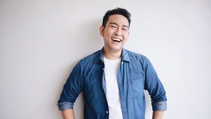 A man in a white t-shirt and blue denim shirt smiling