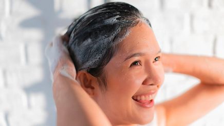Smiling woman washing her hair with clarifying shampoo in the shower.